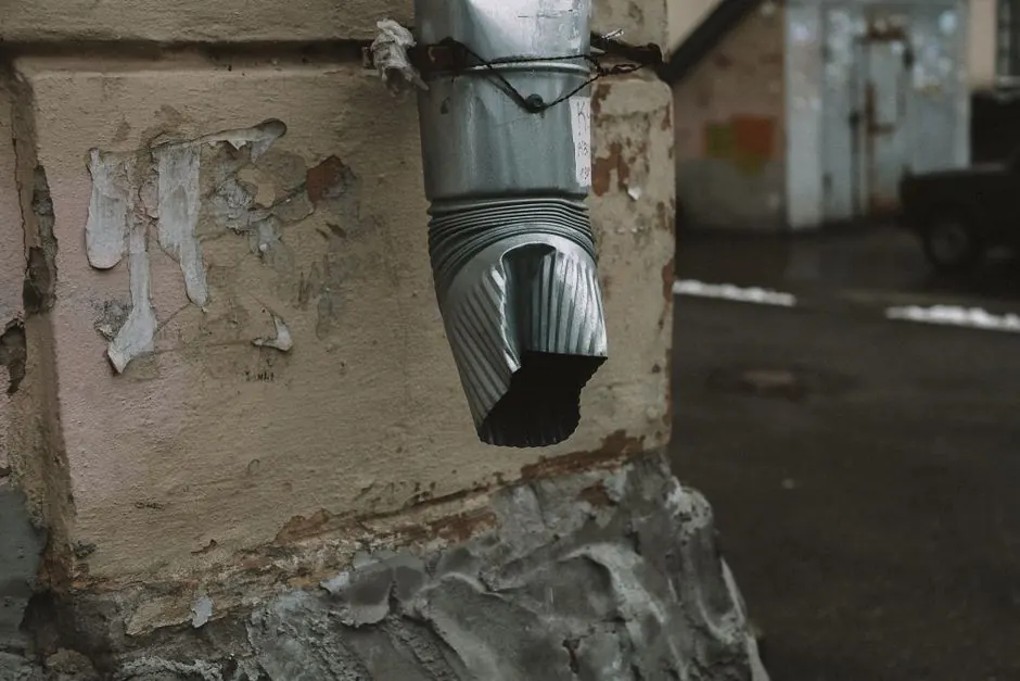 A metal drainage pipe with a rustic appearance on an aged wall with flaking paint.