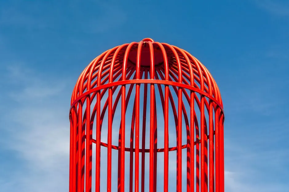 Colorful red birdcage reaching towards the bright blue sky, symbolizing freedom.