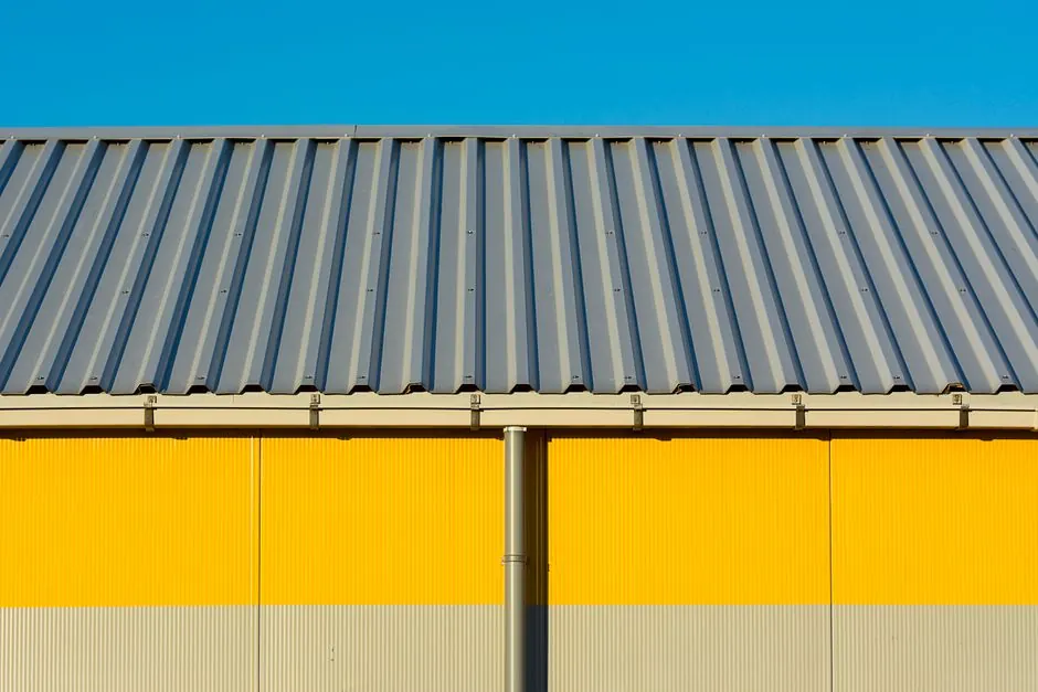 Photo of a yellow warehouse wall with a corrugated metal roof under a clear blue sky.